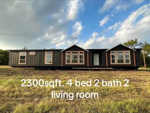 Modern black modular home with large windows set on grass under a blue sky. Text overlay reads "2300 sqft, 4 bed, 2 bath, 2 living room."