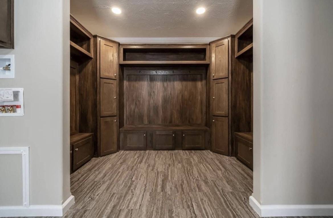 Spacious mudroom with dark wood cabinetry, bench seating, and storage. Recessed lighting casts a warm glow on the light wood floor, creating a welcoming atmosphere.