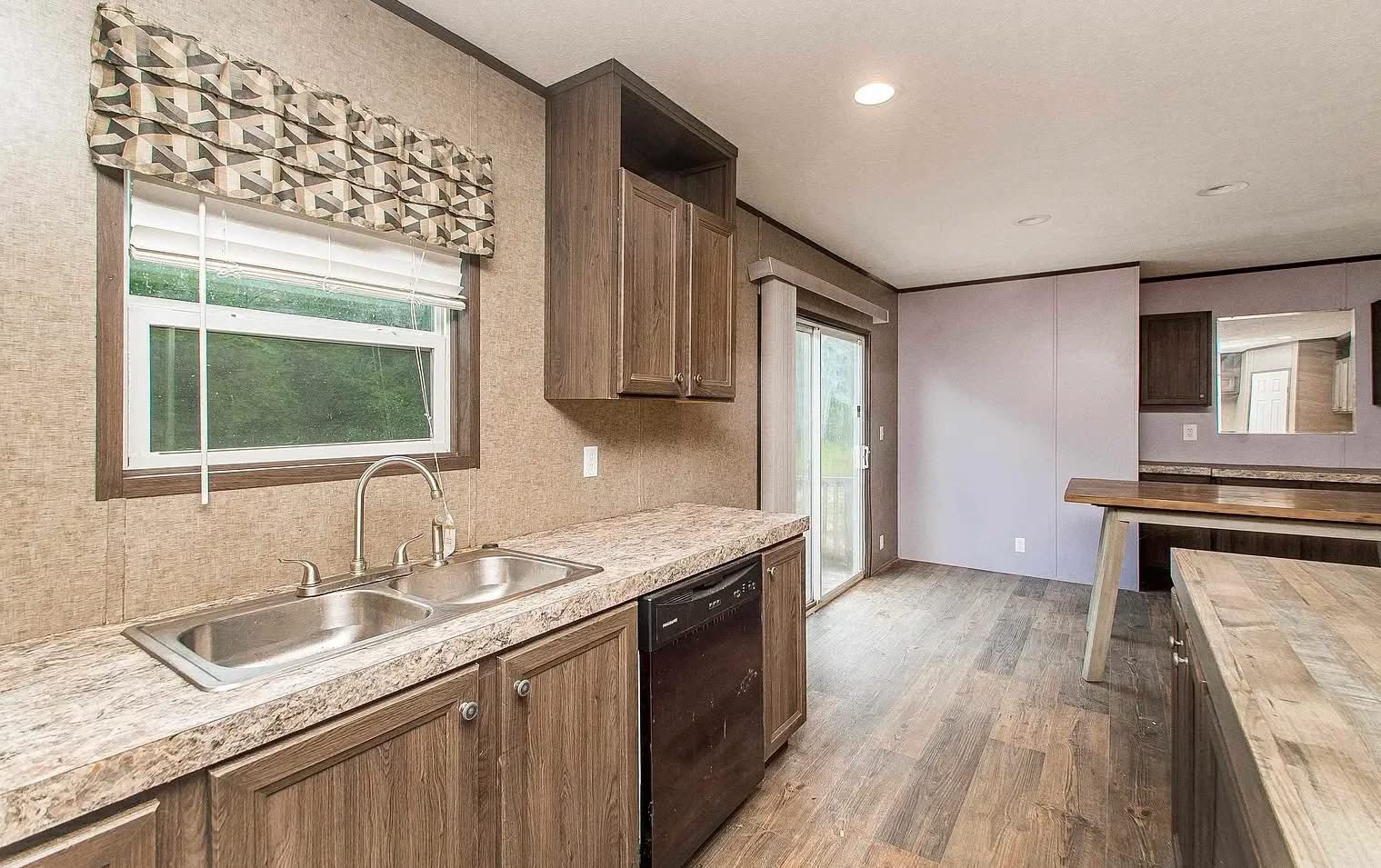 Spacious kitchen with wooden cabinets, marble countertops, and dual sink. Natural light flows through a window and glass sliding door onto wood floors.
