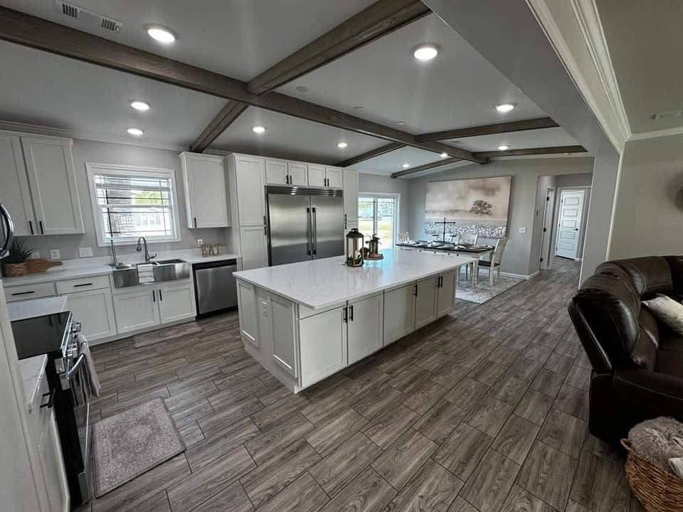 Spacious, modern kitchen with white cabinets, large island, stainless steel appliances, wood beam ceiling, and dining area in an open, airy setting.