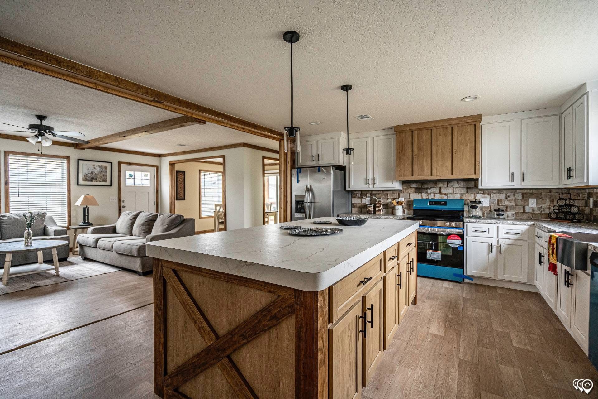 Spacious open-concept kitchen and living area with rustic wood accents. Features large island, modern appliances, cozy sofa, and wood-beam ceiling.