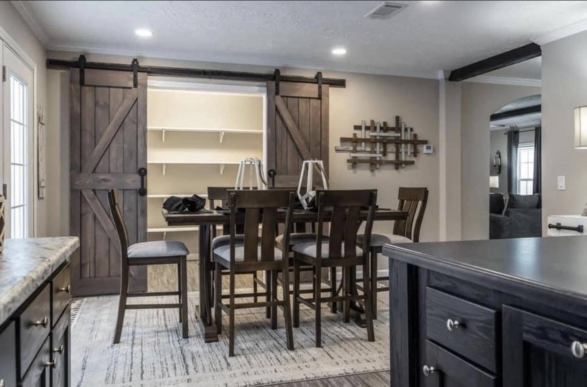 Dining area with a dark wooden table and high-back chairs on a patterned rug. Barn doors on rails reveal a closet. Cozy and rustic ambiance.