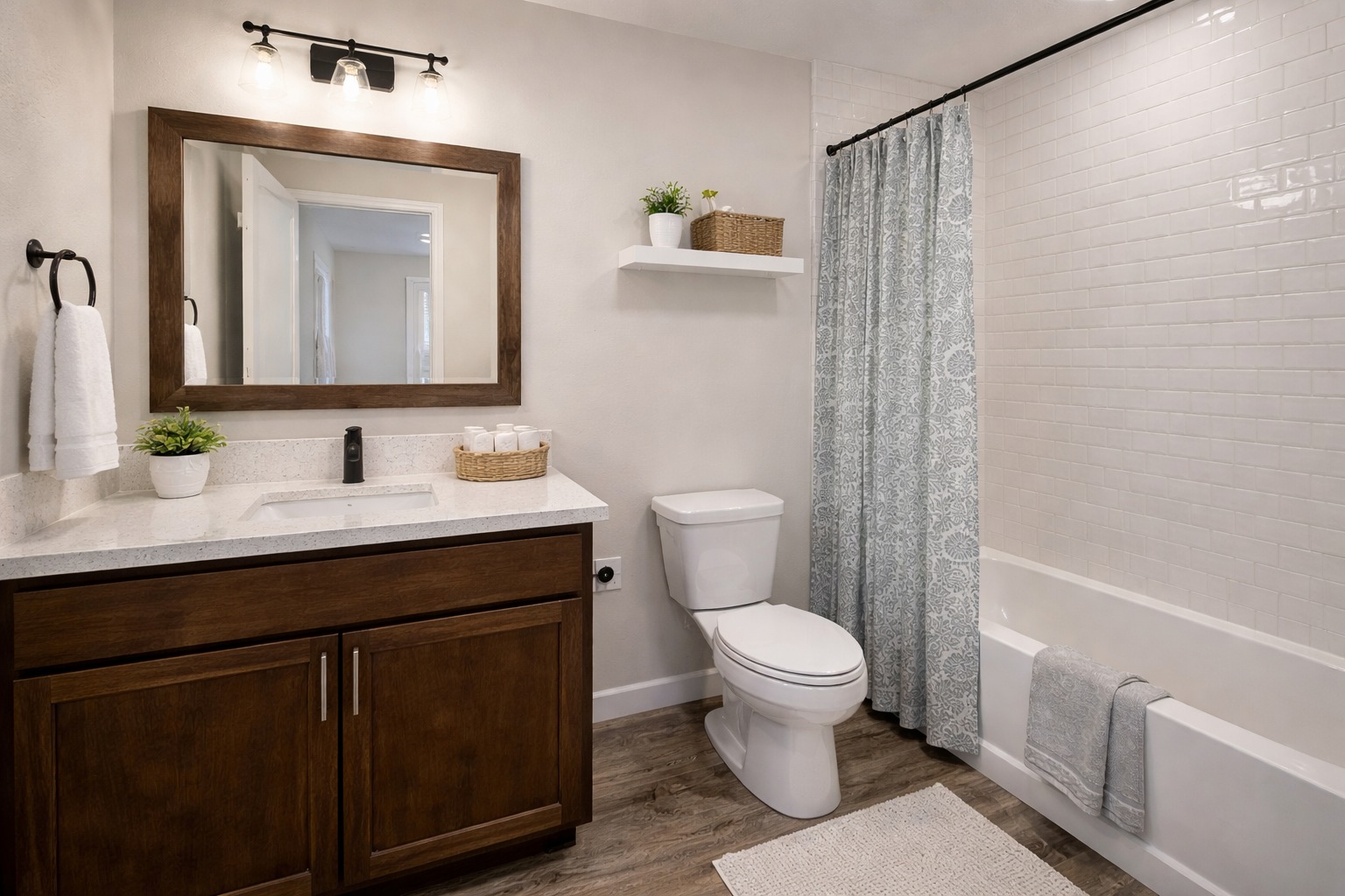 A modern bathroom features a wooden vanity with a white countertop, a large mirror, potted plants, and a towel. A tub with a blue curtain is on the right.
