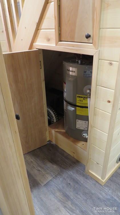  Tiny house interior with wooden staircase cabinet revealing Reliance water heater featuring EnergyGuide label, efficient utility storage design, rustic wood paneling, compact living solution, and smart space-saving architecture for modern sustainable homes.